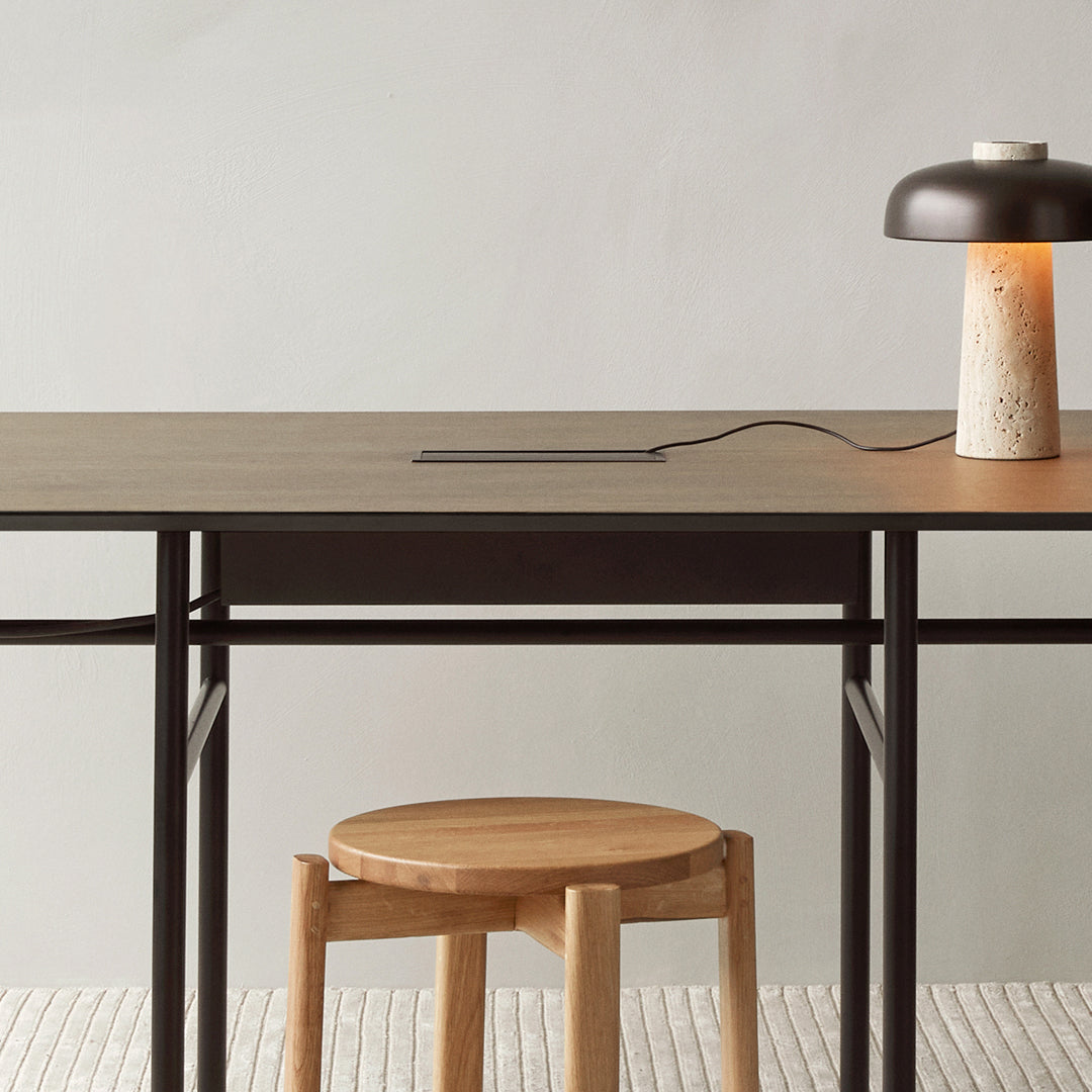Modern desk featuring a muted gray surface, sleek black metal frame, and a warm wooden stool against a soft beige backdrop.