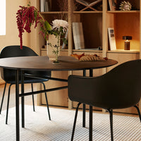 Modern black dining chairs and round brown table on a textured, neutral-toned rug in a stylish interior setting.