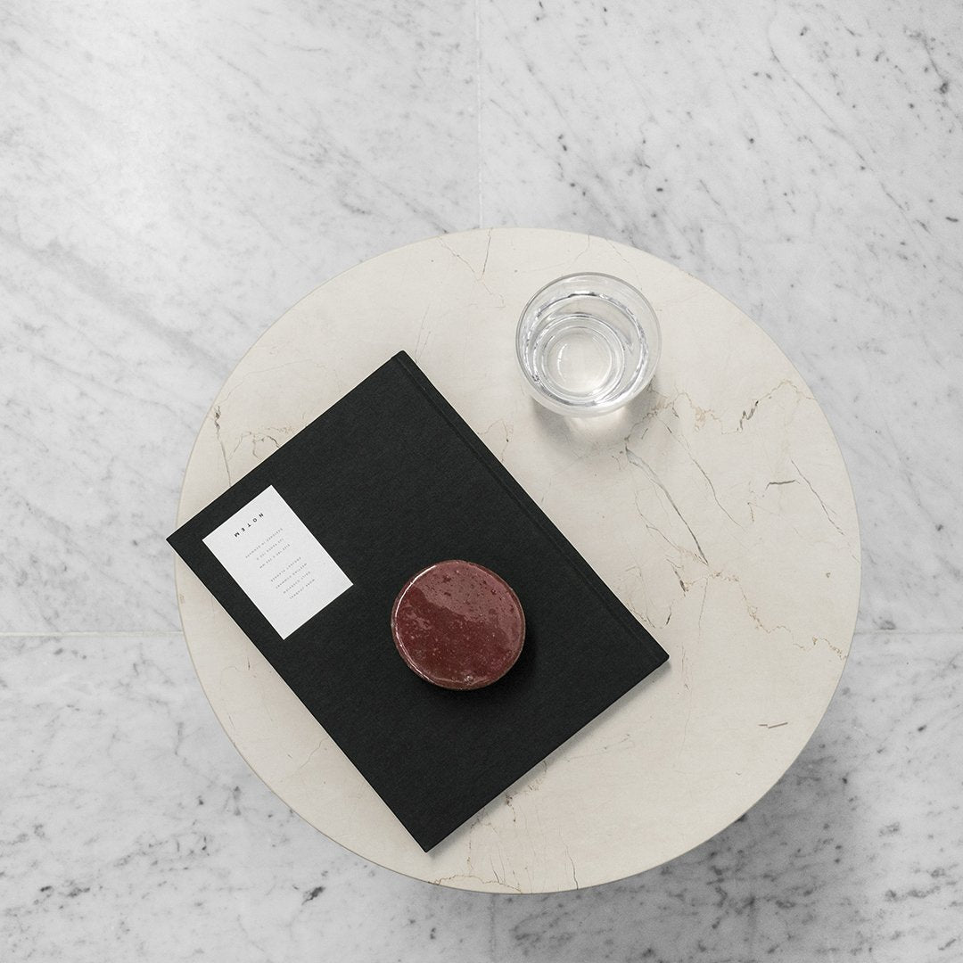 Black notebook with white label, circular maroon coaster on a light marble table, clear glass of water beside.