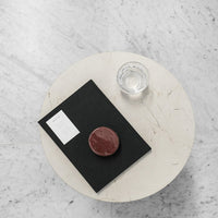 Black notebook with white label, circular maroon coaster on a light marble table, clear glass of water beside.