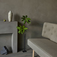 "Soft gray sofa with tufted pattern, green plant, textured gray wall, and minimalist decor elements in muted colors."