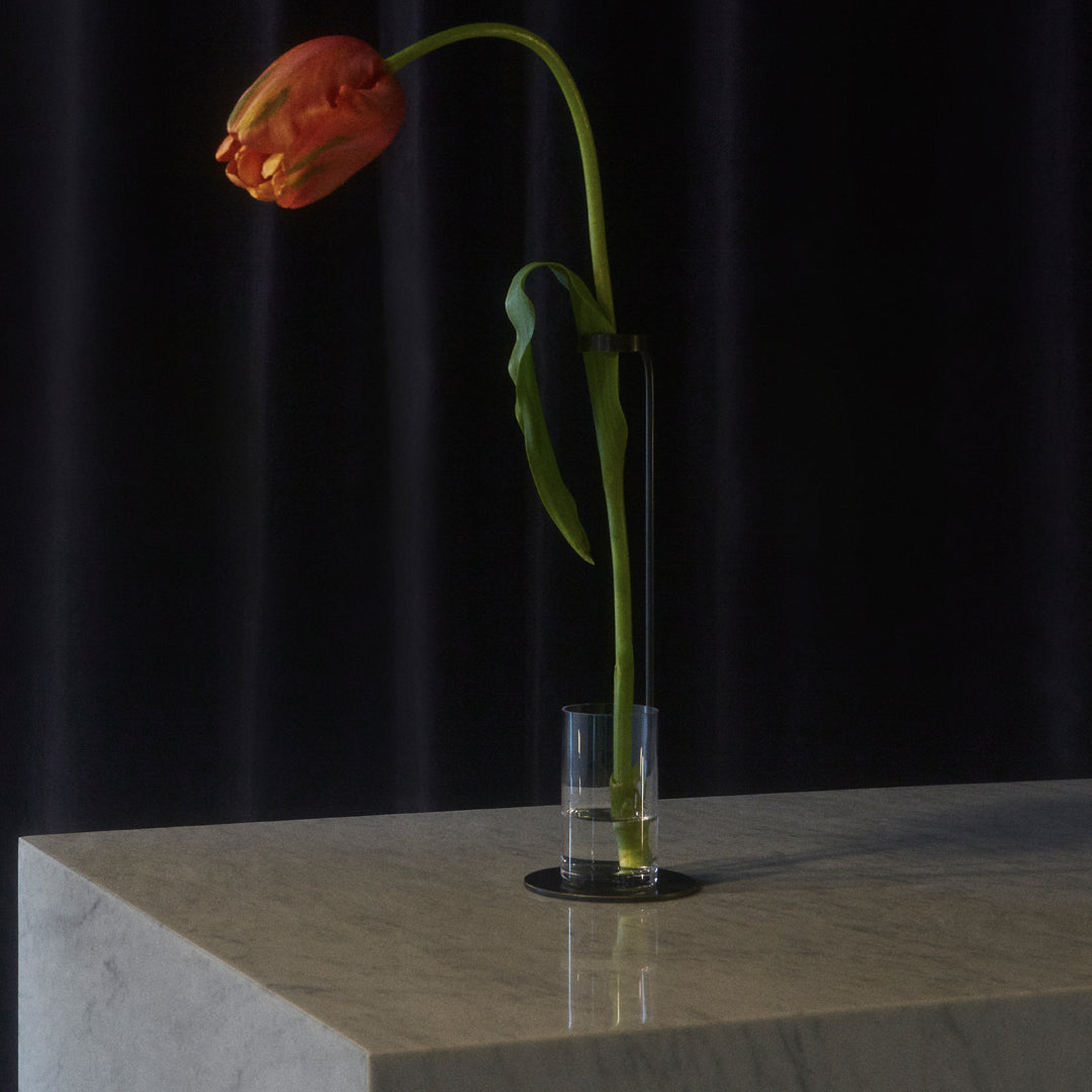Single orange tulip in a clear glass vase, set against a dark textured background, on a sleek marble surface.