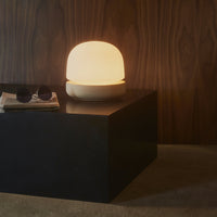 Modern lamp with a circular white shade, soft warm glow, and a minimalist black base on a textured surface.