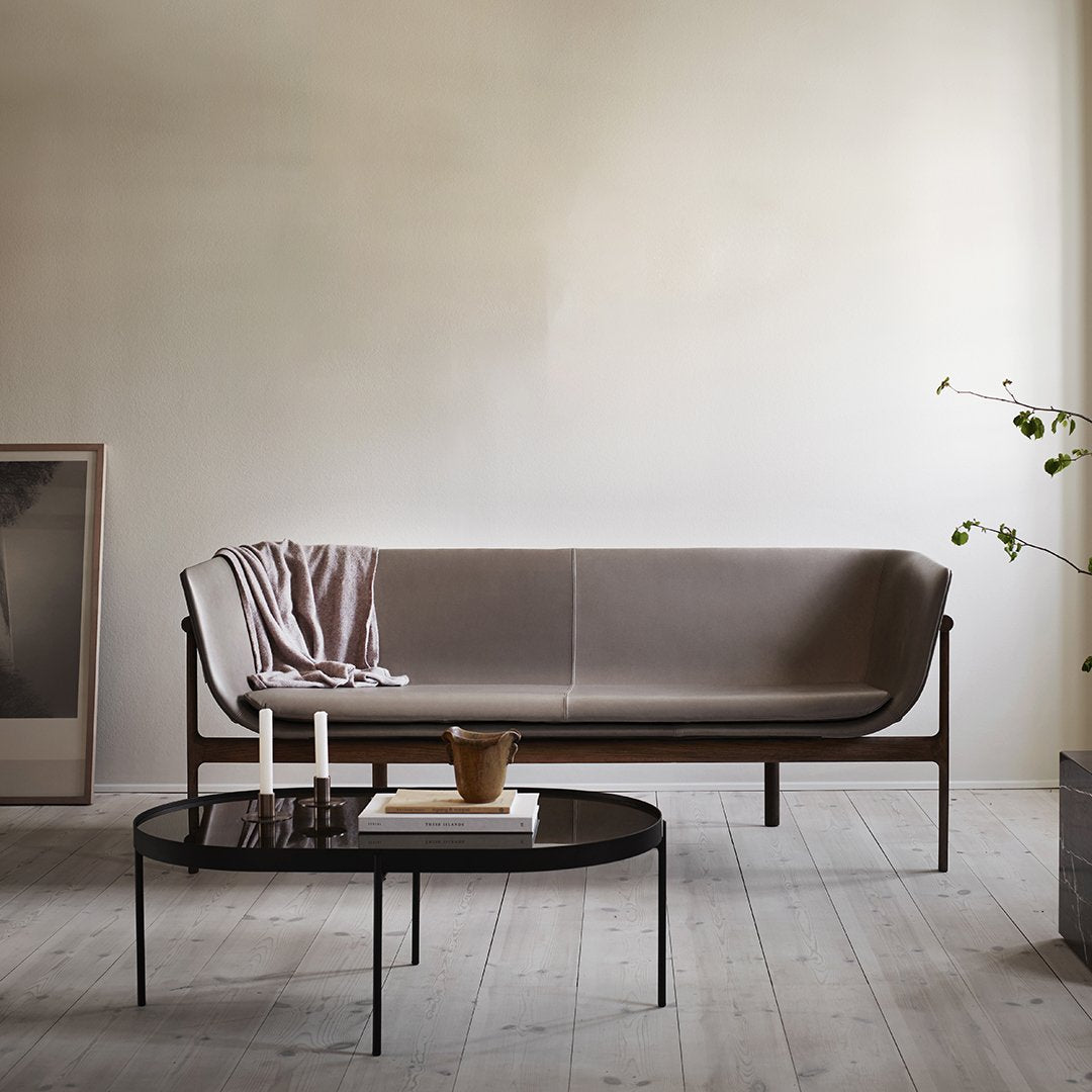Modern taupe sofa with soft texture and sleek wood legs, paired with a minimal black oval coffee table.
