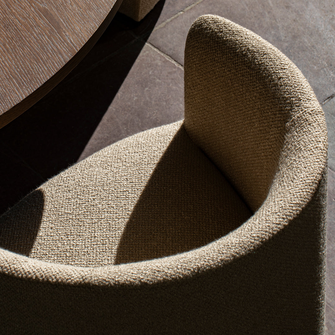 Textured beige armchair with a curved design, featuring light and shadow interplay on a dark tiled floor.