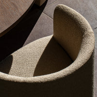 Textured beige armchair with a curved design, featuring light and shadow interplay on a dark tiled floor.