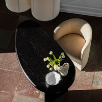 Elegant black wood table with natural grain, paired with a soft cream upholstered chair on textured tile flooring.