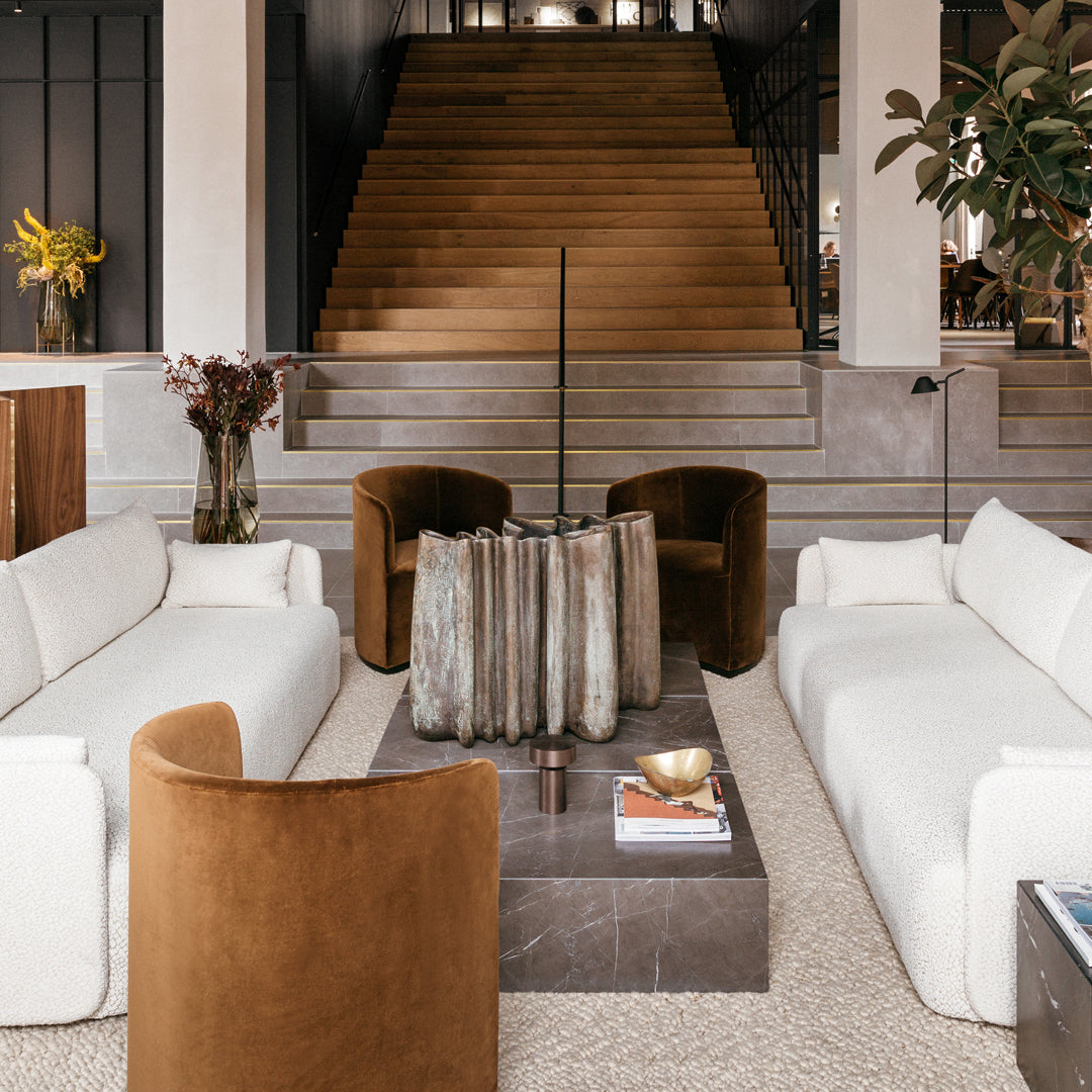 Modern living room featuring white sofas, rust-colored chairs, a textured grey coffee table, and natural wood accents.