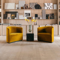 "Modern yellow velvet chairs with curved design, set against a minimalist wooden backdrop and a chic black accent table."