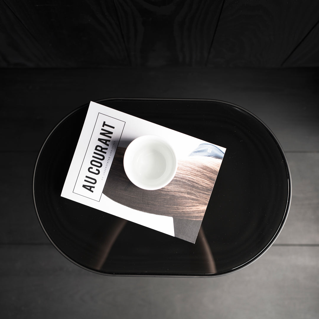 Black oval table featuring a glossy finish, a white bowl, and a magazine with a clean, minimalistic design.