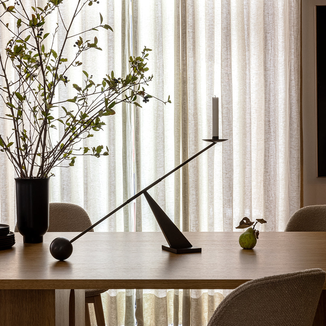 "Modern black candle holder with geometric design against neutral-toned background and soft, textured curtains."