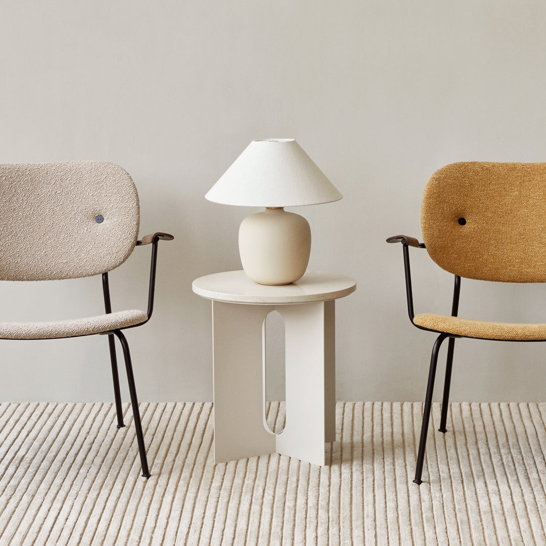 Neutral-toned chairs in beige and mustard, paired with a minimalist white lamp on a light-colored table and striped rug.