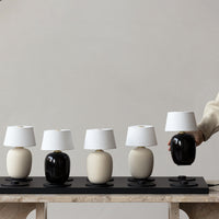 Modern table lamps in black, white, and cream with minimalist designs and cylindrical shapes on a dark display.