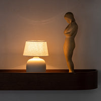 Sleek white lamp with a patterned shade, surrounded by warm wooden tones and a subtle beige statue.