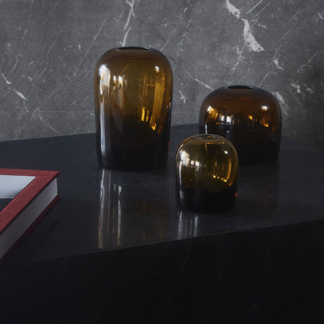 "Set of three amber glass vases with a gradient effect, displayed on a sleek black surface against a marble background."