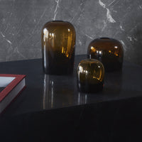 "Set of three amber glass vases with a gradient effect, displayed on a sleek black surface against a marble background."