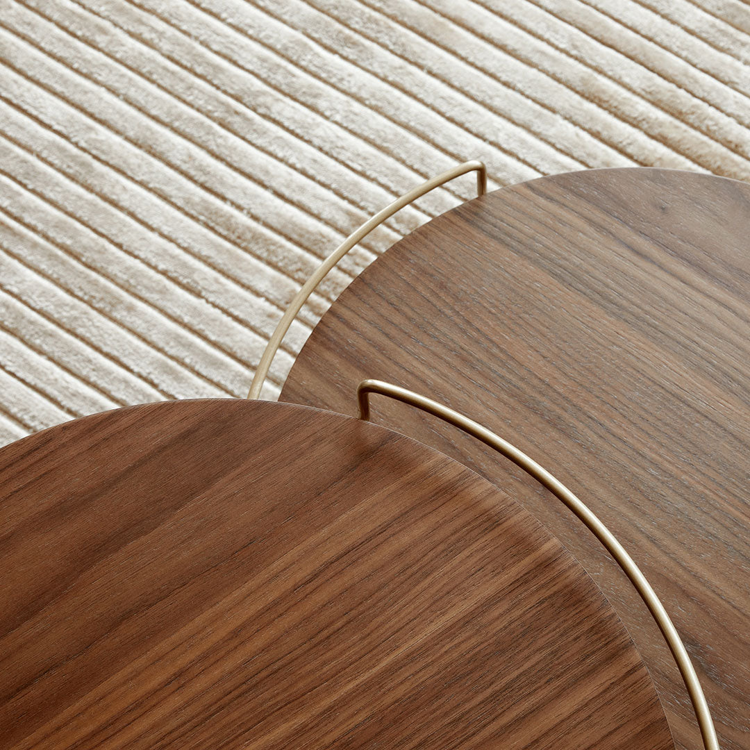 "Brown wooden trays with elegant curved edges and gold handles, set on a textured cream-colored surface."