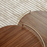 "Brown wooden trays with elegant curved edges and gold handles, set on a textured cream-colored surface."