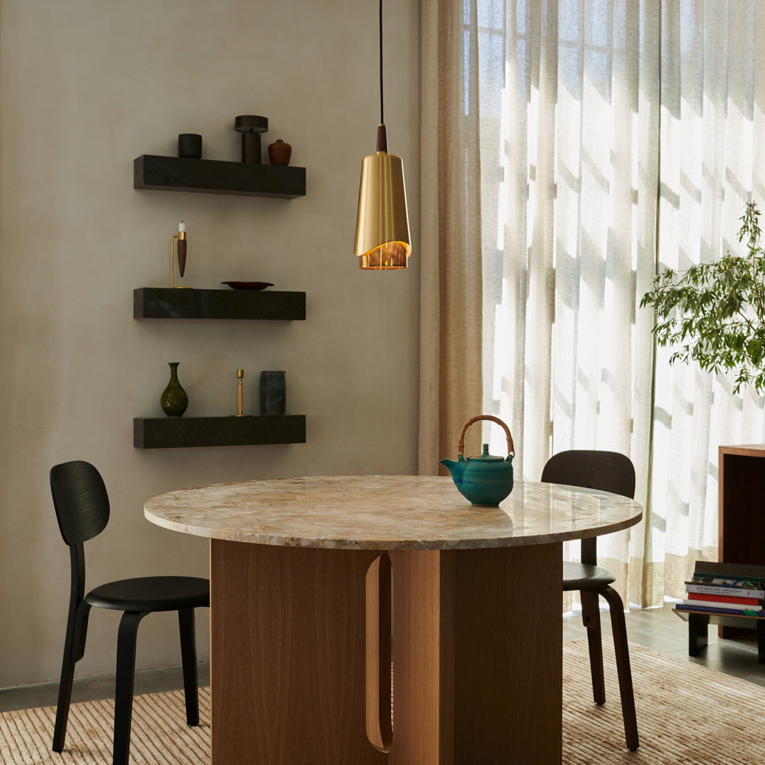 "Modern round marble dining table with warm wood base, black chairs, and gold pendant light against a neutral wall."