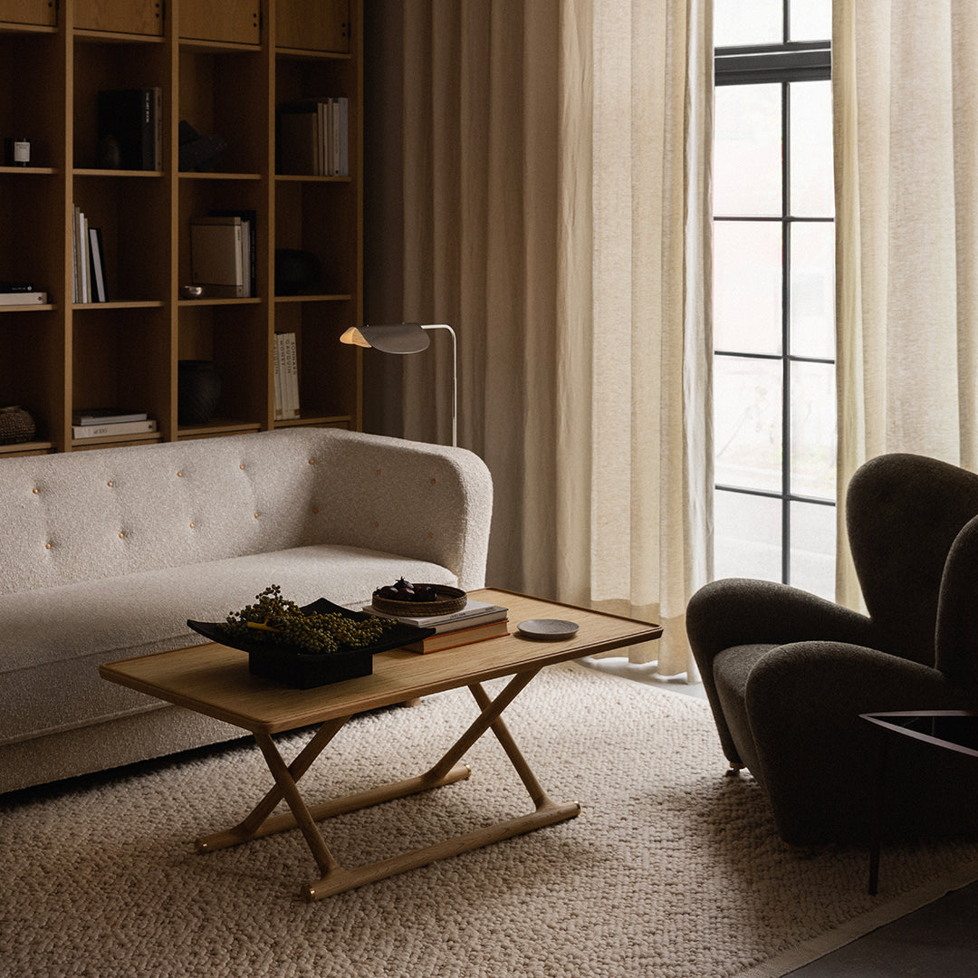 Neutral-toned living room with a beige sofa, soft gray armchair, and light wood coffee table on a textured rug.