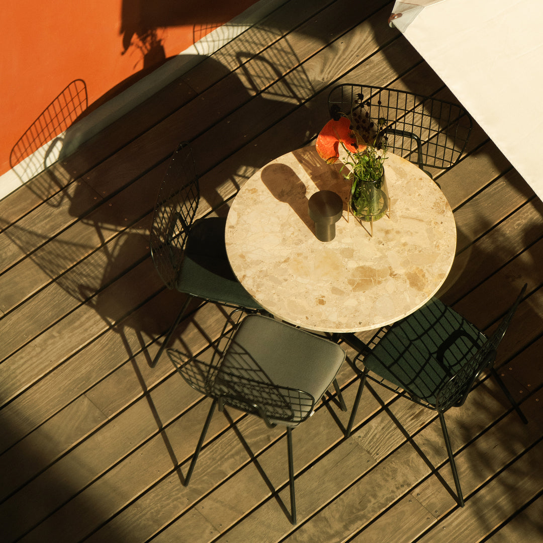 "Round marble table with green and black wire chairs against a warm orange backdrop, showcasing modern outdoor aesthetics."