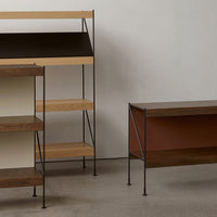 Minimalist shelving units with light wood, dark brown, and rust-colored accents on a textured gray background.