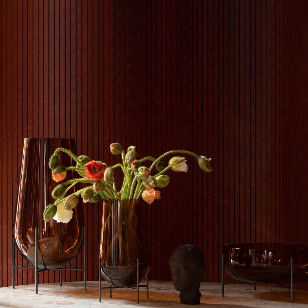 Amber glass vases with colorful floral arrangements against a rich brown background and sleek black accents.