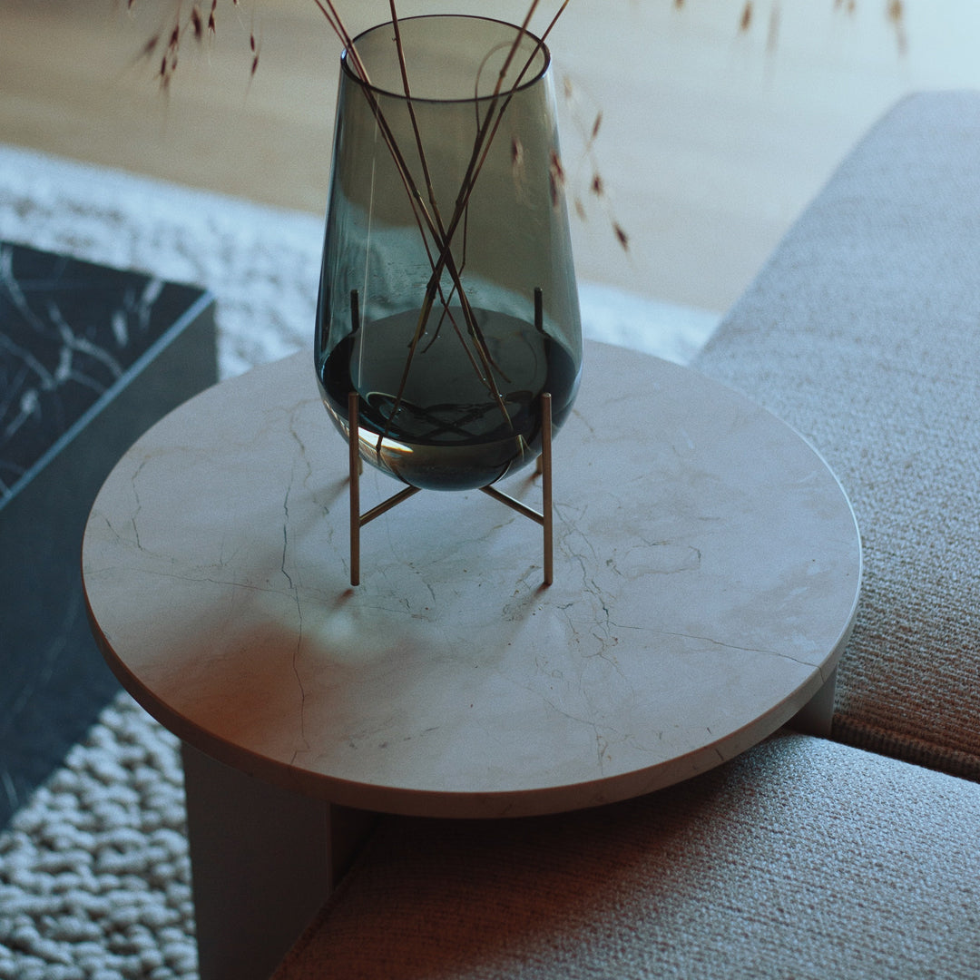 Elegant round marble tabletop in a soft white with subtle gray veining, topped with a dark green glass vase.