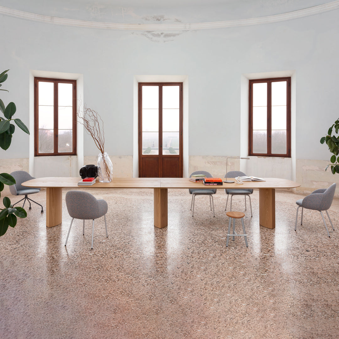 Modern minimalist room with light grey chairs, a wooden table, and soft natural light against pale walls and terrazzo floor.