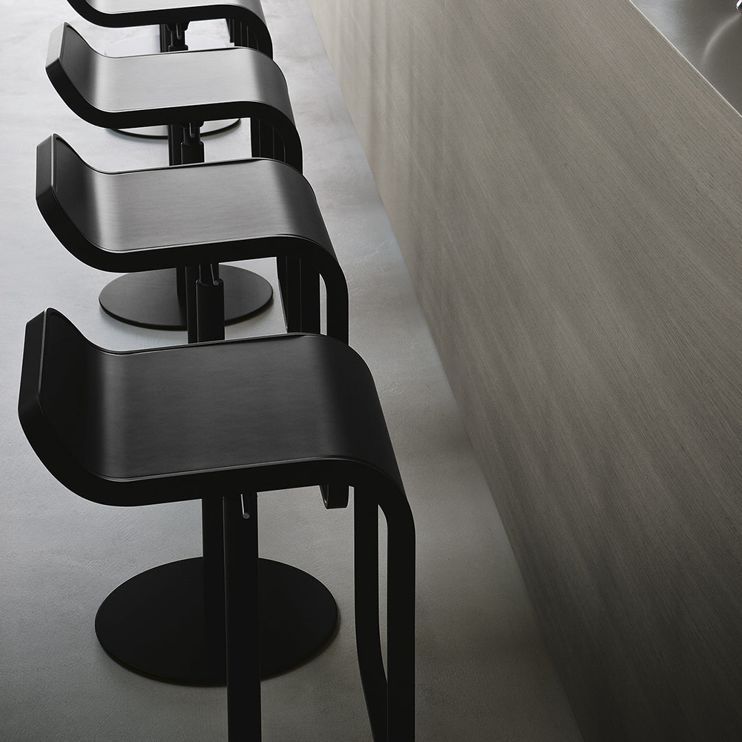 Black modern bar stools with curved seats and round bases against a light wood backdrop. Sleek, minimalist design.