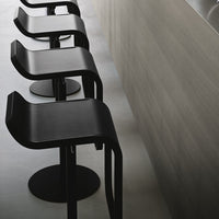 Black modern bar stools with curved seats and round bases against a light wood backdrop. Sleek, minimalist design.