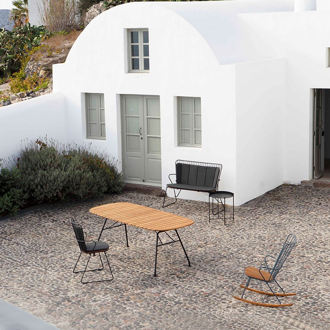 "Rustic outdoor furniture with natural wood tones and black metal accents against a whitewashed building and stone patio."