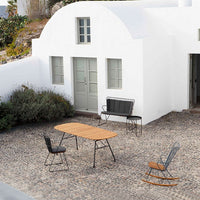 "Rustic outdoor furniture with natural wood tones and black metal accents against a whitewashed building and stone patio."