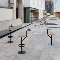 Modern outdoor barstools with natural wood seats and sleek black and white metal bases, set on a textured stone patio.