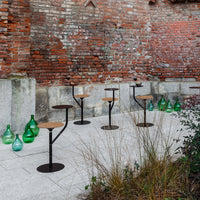 Stylish black metal bar stools with wood seats, set against a rustic red brick wall and surrounded by green glass accents.