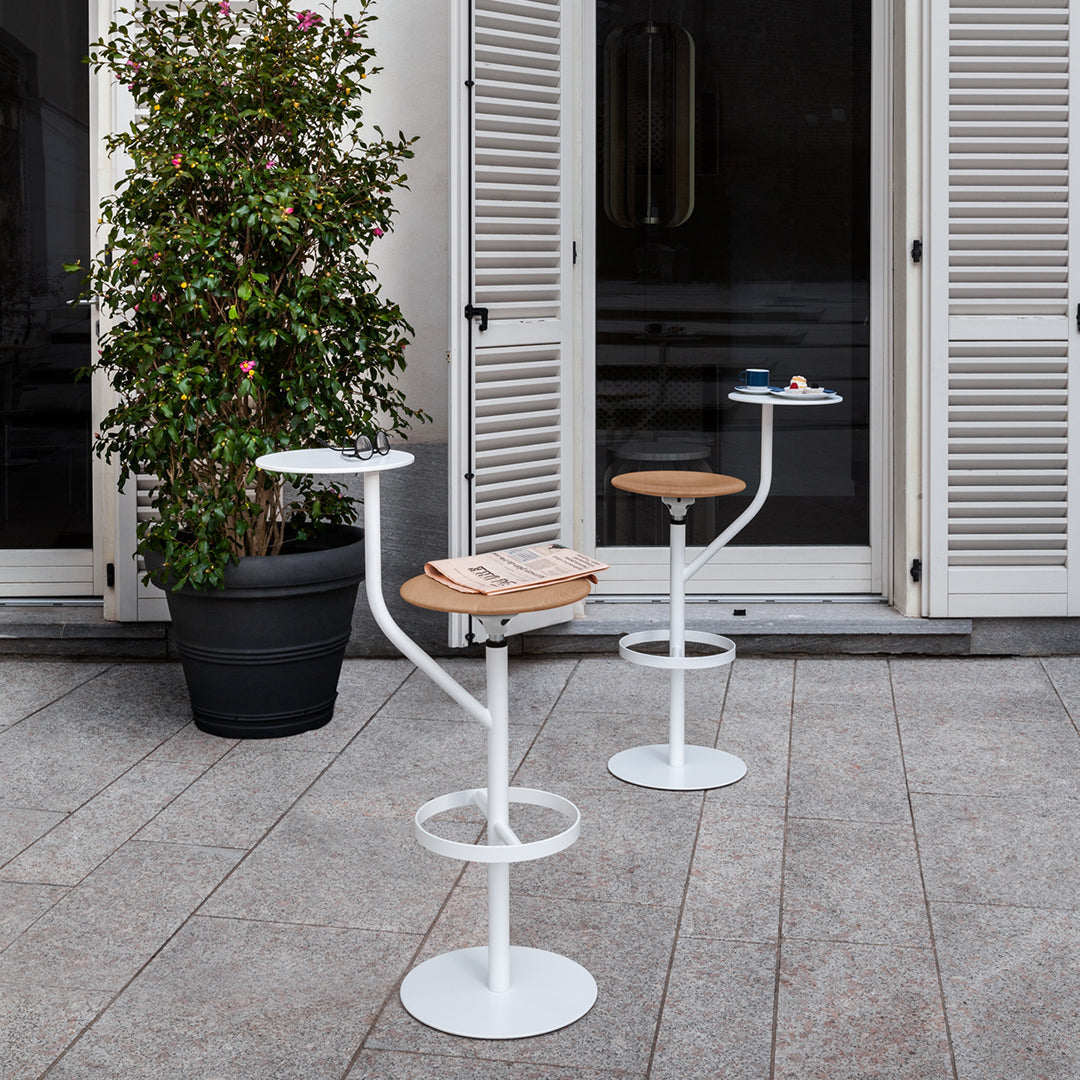 Modern white bar tables with circular bases and wooden tops, featuring sleek lines and a stylish outdoor setting.
