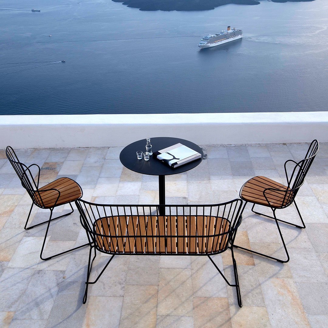 Black metal outdoor furniture with wooden slats, set against a scenic water view and sunny sky.