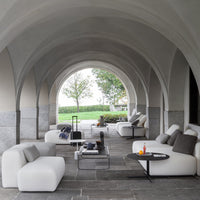 Modern outdoor lounge with sleek white sofas and gray accents, set against a minimalist stone background.