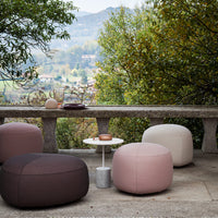 Multicolored poufs in soft pink, white, and dark brown, arranged outdoors with a scenic backdrop.