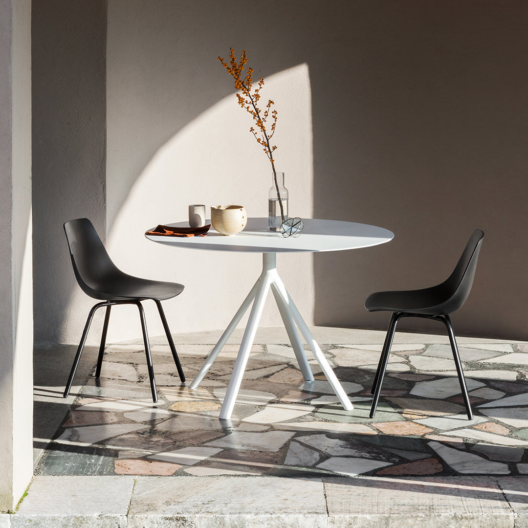 Modern round white table with black chairs on a patterned stone floor, set against a soft beige wall.
