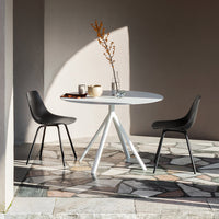 Modern round white table with black chairs on a patterned stone floor, set against a soft beige wall.