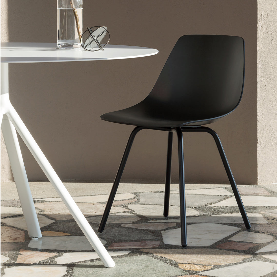 Black minimalist chair with a smooth, matte finish, set against a textured stone floor and a white table.