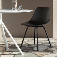 Black minimalist chair with a smooth, matte finish, set against a textured stone floor and a white table.
