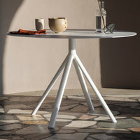 Modern round table with a sleek white finish and unique tripod base, set against a textured stone floor.
