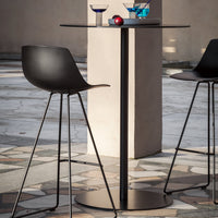 Black bar table and stools with minimalist silhouette, set against a textured stone floor pattern.