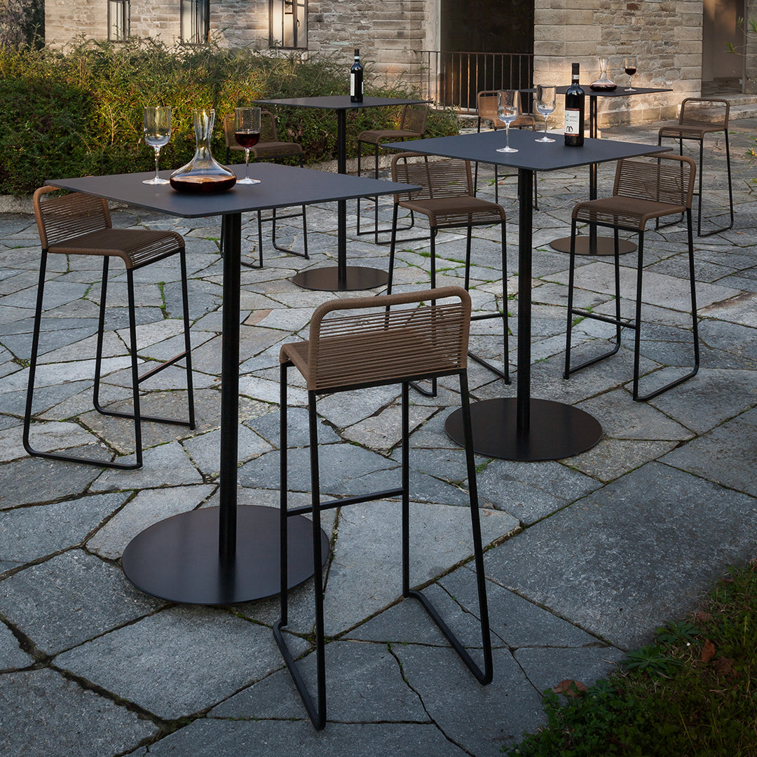 Outdoor bar tables and chairs in black metal with wood accents, set on a patterned stone patio.  