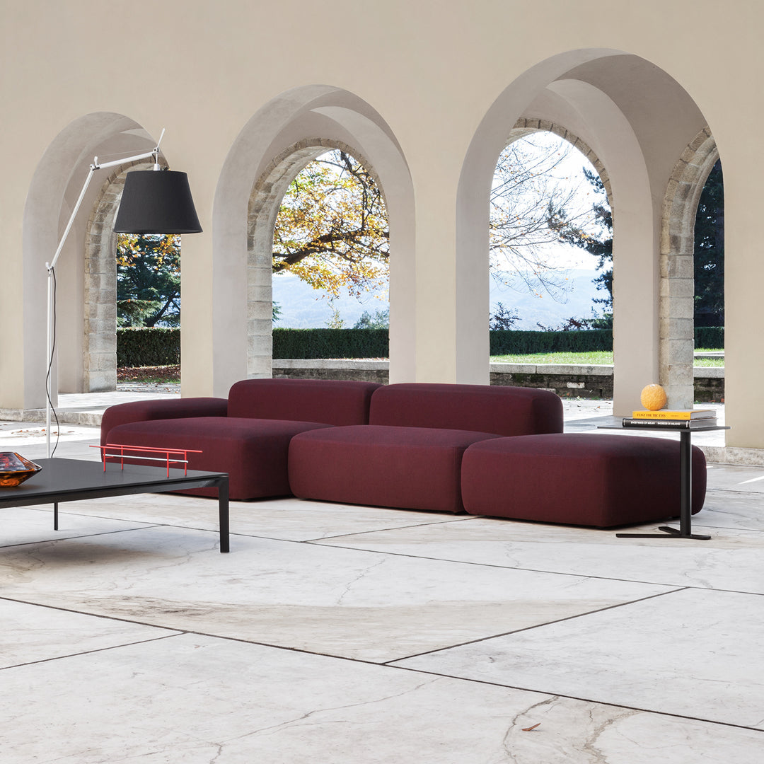 Modern burgundy modular sofa with smooth, rounded shapes, set against a minimalistic, neutral-toned interior.