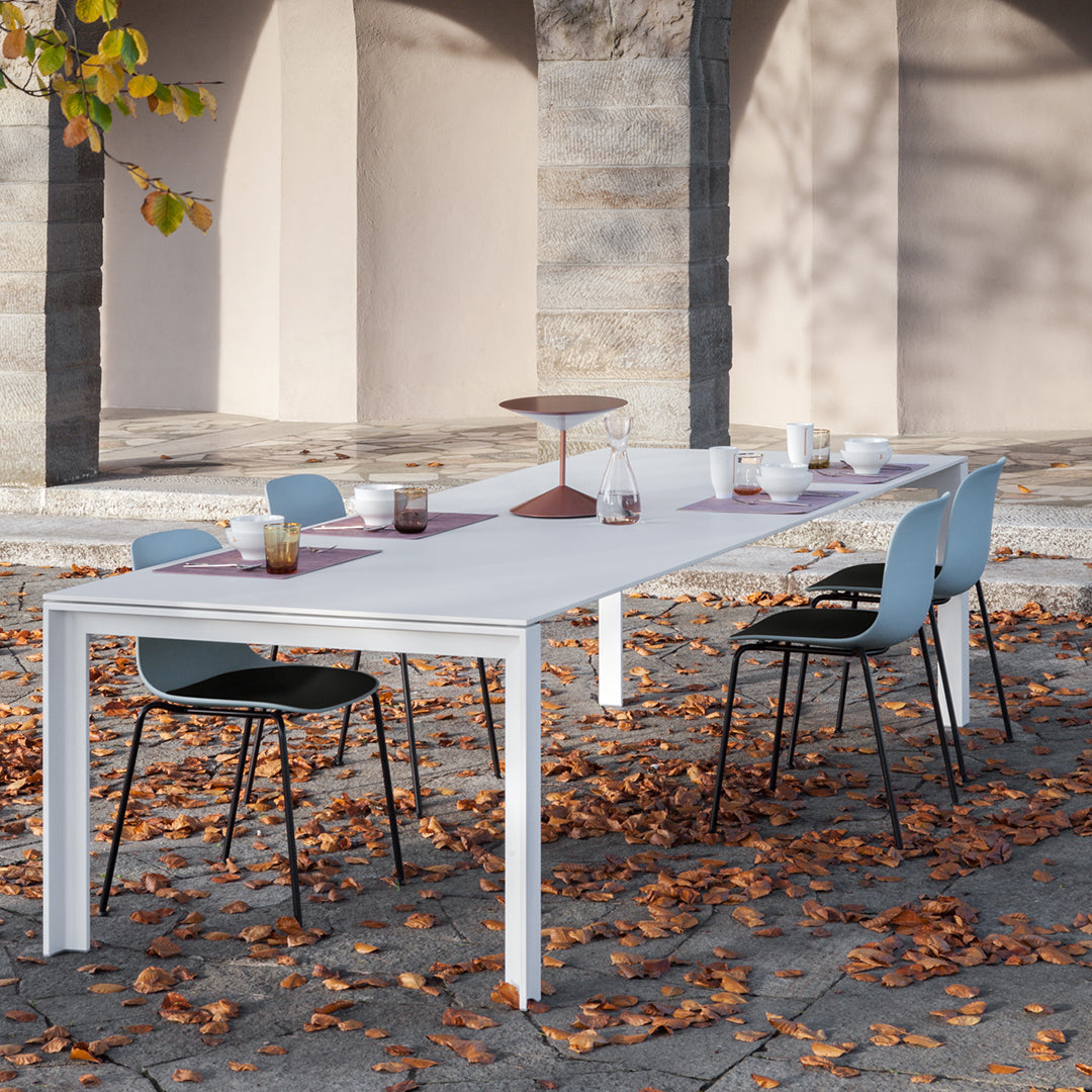 Modern white table with gray and black chairs, accented by a maroon table runner, surrounded by autumn leaves.