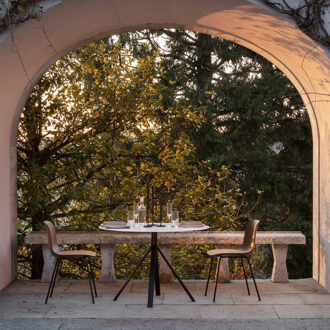 "Round black table with minimalist design, surrounded by natural greens and warm sunset hues."