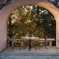 Elegant outdoor dining set with neutral tones, featuring a round table and minimalist chairs against a warm, natural backdrop.